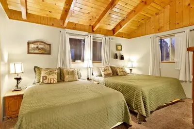 two beds in a bedroom with wooden ceilings and windows at Pine Cone Cottage by Big Bear Vacations Adorable Walk To Lake Furnished Chalet in Big Bear Lake