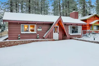 a red house with snow in front of it at Pine Cone Cottage by Big Bear Vacations Adorable Walk To Lake Furnished Chalet in Big Bear Lake
