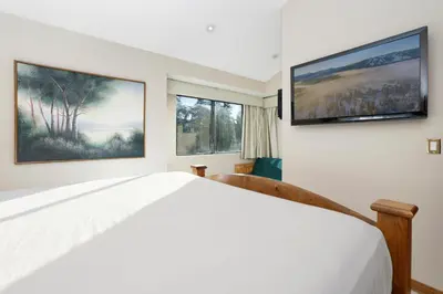 a bedroom with a white bed and two windows at Forest Shores Lake View Condo by Big Bear Vacations Lakefront Village in Big Bear Lake