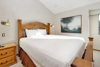 a bedroom with a large white bed and a table at Forest Shores Lake View Condo by Big Bear Vacations Lakefront Village in Big Bear Lake