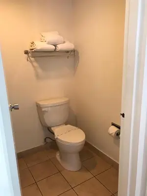 a bathroom with a toilet and towels on a shelf at Ramada by Wyndham Torrance in Torrance
