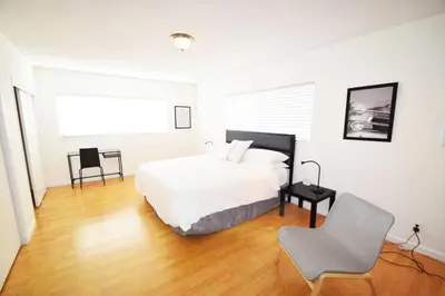a white bedroom with a bed and a chair at Hollywood Business Apartments in Los Angeles