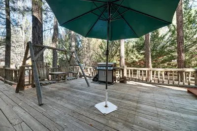 a green umbrella on a wooden deck with a trash can at Abe's Cool Cabin - Nice luxury home with a game room, hot tub, and pool table in Big Bear Lake