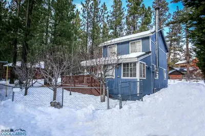 a blue house in the snow with a fence at Apples Delight -WALK TO THE LAKE! Enjoy the huge backyard with lovely forest views ! in Big Bear Lake