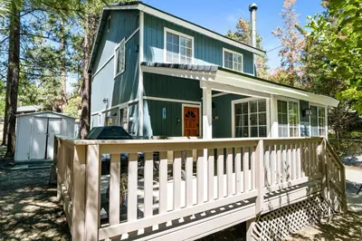 a green house with a white fence at Apples Delight -WALK TO THE LAKE! Enjoy the huge backyard with lovely forest views ! in Big Bear Lake