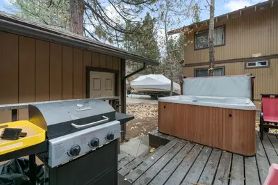 a grill and a hot tub on a deck next to a house at Bear Retreat - Modern location within walking distance to Snow Summit with a private hot tub! in Big Bear Lake