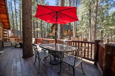 a table and chairs on a deck with a red umbrella at Catalina Creekside Cabin - Log home with wood burning fireplace for an immersive mountain getaway! in Big Bear Lake