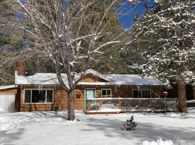 a house in the snow with a tree in front of it at Catalina Retreat -Cozy mountain home in a tree filled neighborhood, plenty of games and a hot tub! in Big Bear Lake