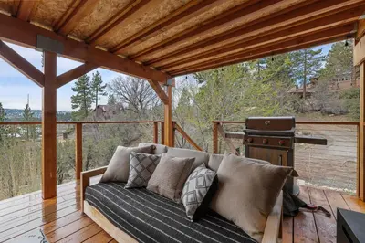 a couch on a wooden deck with a grill at Enchanted Hideaway - Newly remodeled with Hot Tub and Lake Views! in Fawnskin