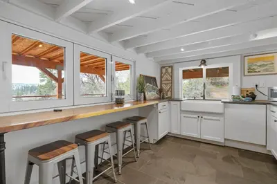 a kitchen with white cabinets and bar stools at Enchanted Hideaway - Newly remodeled with Hot Tub and Lake Views! in Fawnskin