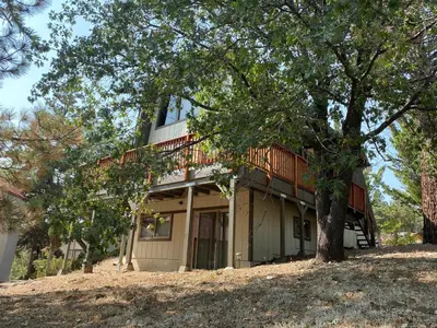 a house on a hill with a tree at Fawnskin Family Cabin - Nicely decorated cabin with a lake view and a Foosball Table! in Fawnskin