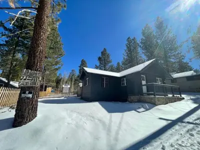 a house in the snow next to a tree at Finns Fish Camp - Walking distance to Lake and Village! Back patio with barbecue, fully fenced yard! in Big Bear Lake