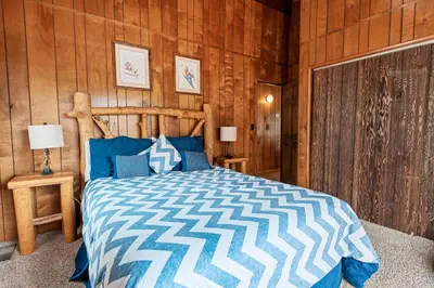 a bedroom with a bed with a wooden wall at Forest Edge Retreat - Cozy, log cabin with a wood burning fireplace! Pool Table, Foosball and Darts! in Big Bear City