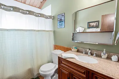 a bathroom with a toilet and a sink and a mirror at Forest Edge Retreat - Cozy, log cabin with a wood burning fireplace! Pool Table, Foosball and Darts! in Big Bear City