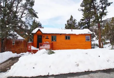 a cabin in the snow with a pile of snow at Forest Edge Retreat - Cozy, log cabin with a wood burning fireplace! Pool Table, Foosball and Darts! in Big Bear City