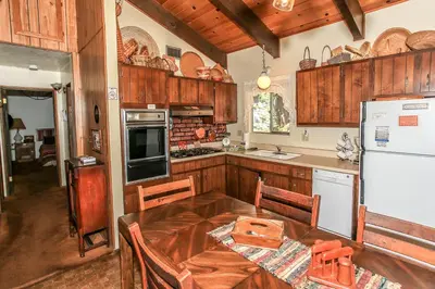 a kitchen with a table and a white refrigerator at Gallagher's West - Pine surrounded deck and barbecue! Bumper Pool and Wet bar! Darts! in Big Bear Lake
