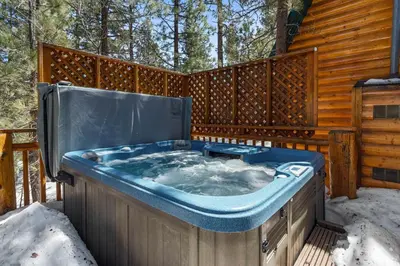 a jacuzzi tub in the snow next to a cabin at Ivvy Bear Lodge - Charming log cabin with Hot tub! Short walk to Village! in Big Bear Lake