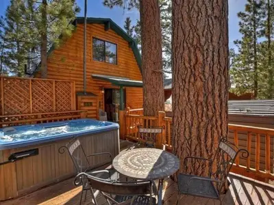 a deck with a table and a tree and a hot tub at Ivvy Bear Lodge - Charming log cabin with Hot tub! Short walk to Village! in Big Bear Lake