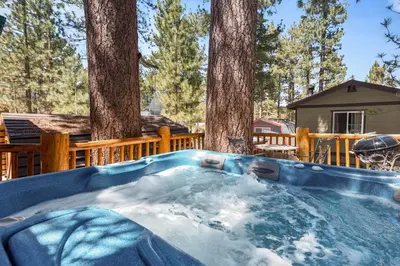 a hot tub with snow in front of trees at Ivvy Bear Lodge - Charming log cabin with Hot tub! Short walk to Village! in Big Bear Lake