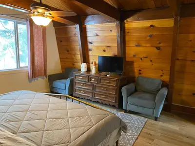a bedroom with a bed and two chairs and a television at The Cozy Bear Cabin - Updated gambrel with huge outdoor space! Cornhole, Tether ball, Fire pit! in Big Bear Lake