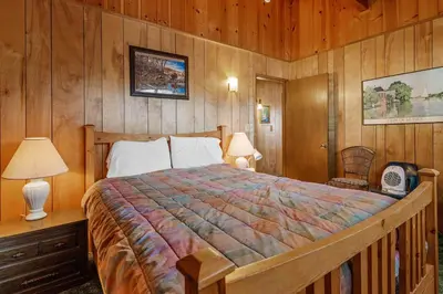 a bedroom with a bed and a wooden wall at Snowridge - Charming classic cabin with a wood burning fireplace and WiFI! in Big Bear City