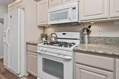 a white kitchen with a stove and a refrigerator at Serenity Knoll - Comfortable, spacious single-level cabin! Newly remodeled! Hot Tub and Pool Table! in Big Bear Lake