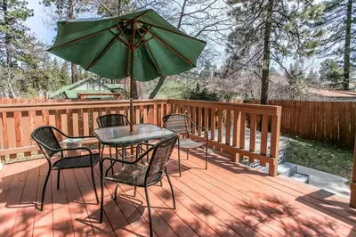 a table and chairs with an umbrella on a deck at Rincon Cabin - Close to the lake with a huge fenced in yard! Hot tub and deck with barbecue! in Big Bear Lake