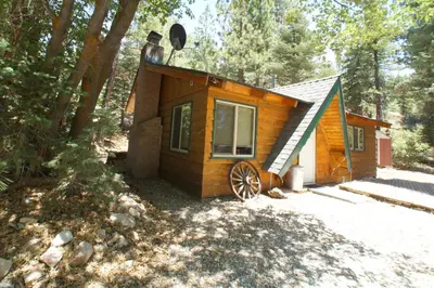 a small cabin in the woods with a wheel at Owl Cabin - Sierra style cabin located on a quiet road in Fawnskin and backs up to National Forest! in Fawnskin