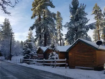 a cabin with snow on the roof next to a road at Pine Forest Cabin - Adorable vintage cabin with a cozy wood burning fireplace and foosball table! in Big Bear Lake