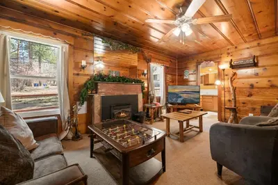a living room with a fireplace and a table at Pine Forest Cabin - Adorable vintage cabin with a cozy wood burning fireplace and foosball table! in Big Bear Lake