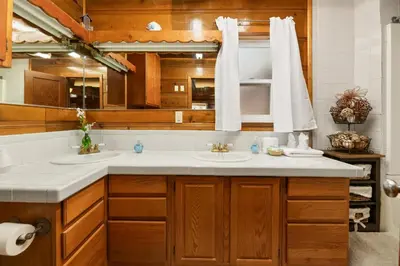 a bathroom with two sinks and wooden cabinets at Pine Forest Cabin - Adorable vintage cabin with a cozy wood burning fireplace and foosball table! in Big Bear Lake