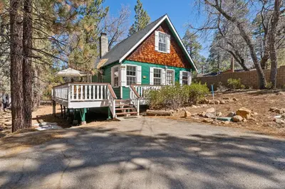 a green house with an orange roof and a porch at Oak Nesting - Great chalet style cabin at the end of the street with rustic stone gas log fireplace! in Big Bear Lake