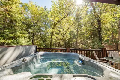 a hot tub on a deck with trees in the background at Bearfoot Bungalow - Premium and spacious home close to the National Forest and The Village! in Big Bear Lake