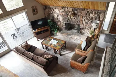 a living room with couches and a stone fireplace at Best View - Spacious home with game room, and 180 degree panoramic view of Big Bear Lake! in Fawnskin