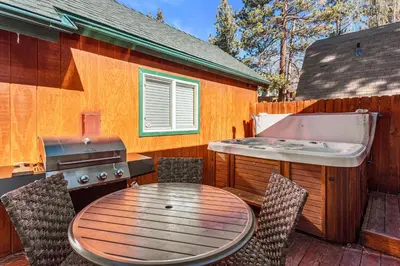 a patio with a table and a hot tub and a grill at Blue Jay Chalet - Classic mountain cabin in one of Big Bear's quietest neighborhoods! in Big Bear Lake