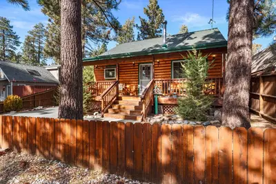 a log cabin with two trees and a fence at Blue Jay Chalet - Classic mountain cabin in one of Big Bear's quietest neighborhoods! in Big Bear Lake