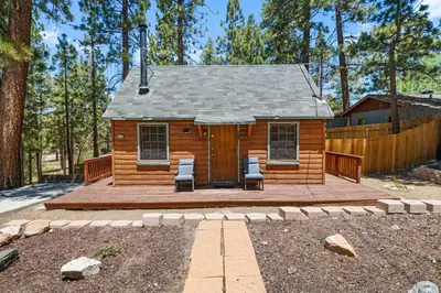 a log cabin with two chairs on a wooden deck at Highland Hideaway - Walk to lake and village! in Big Bear Lake