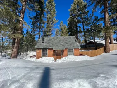 a small house in the snow with a fence and trees at Highland Hideaway - Walk to lake and village! in Big Bear Lake