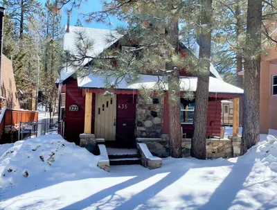 a red cabin with a red door in the snow at Lake Cottage - Vintage Big Bear Cabin close to The Village and Lake in Big Bear Lake
