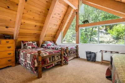 a bedroom with two beds and a window in a log cabin at Moonlight Shores Lakefront - Lakefront home with hot tub! in Fawnskin