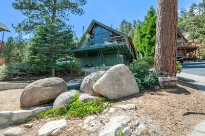 a house with rocks in front of a tree at Moonlight Shores Lakefront - Lakefront home with hot tub! in Fawnskin