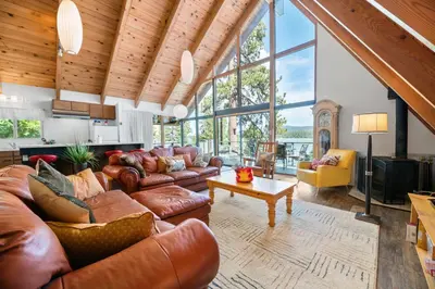 a living room with leather furniture and large windows at Moonlight Shores Lakefront - Lakefront home with hot tub! in Fawnskin