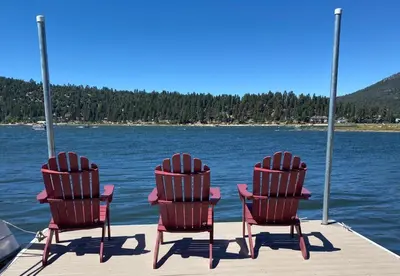 three chairs sitting on a dock on a body of water at Stillwater Cove Lakefront - Breathtaking views, charming vintage cabin, woodsy interior! Boat Dock! in Big Bear Lake