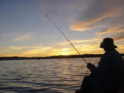 a person fishing on a boat on a lake at sunset at Summit Condo - Luxury condo, walk to the slopes! in Big Bear Lake