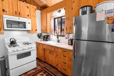 a kitchen with wooden cabinets and a stainless steel refrigerator at The Cuddle Inn - True feeling of a great cabin! Beautiful and homey! Walking distance to the lake! in Big Bear Lake