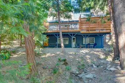 a blue house with a deck in the woods at Steps to Lake Arrowhead Cabin with Full Lake Access in Lake Arrowhead
