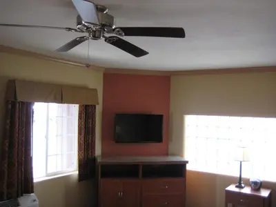 a living room with a ceiling fan and two windows at Americas Best Value Inn - Porterville in Porterville