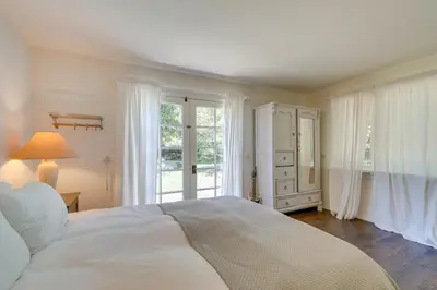 a white bedroom with a large bed and windows at Farmhouse-Chic Carpinteria Cottage with Pool Access in Carpinteria
