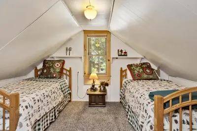a attic bedroom with two beds and a window at Moonridge R n R- Cozy Single Level Central Chalet Home in Big Bear Lake