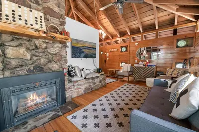 a living room with a fireplace and a stone wall at Clerestory Cottage - The perfect cozy getaway with a hot tub in Big Bear Lake